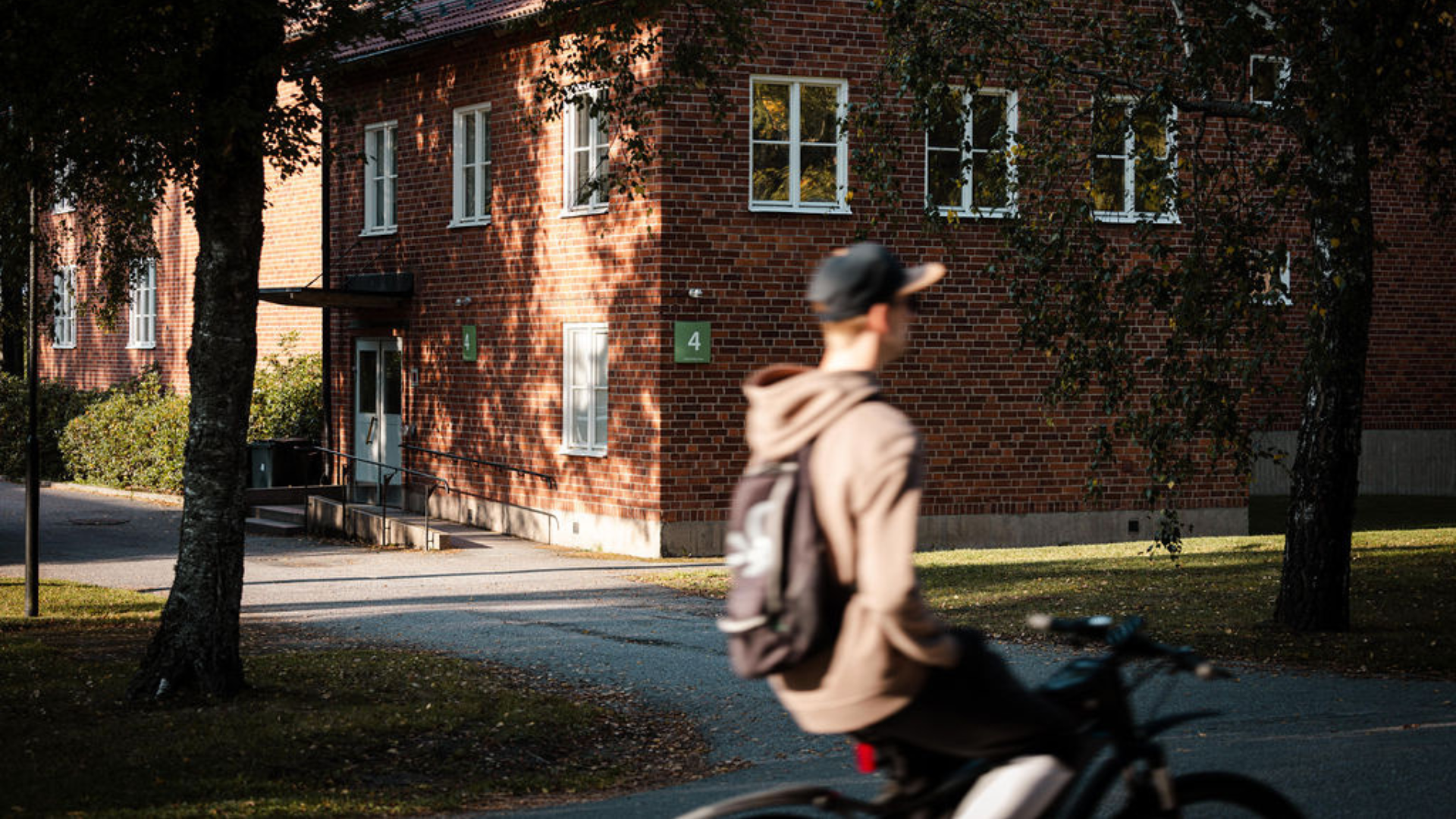 Manlig cyklist i förgrunden som cyklar förbi ett tegelhus på Campus Roslagen.